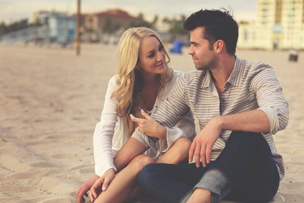 Casal apaixonado sentado na praia olhando um para o outro
