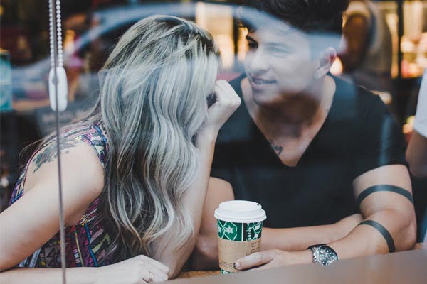 Foto de casal conversando e rindo enquanto tomam um café