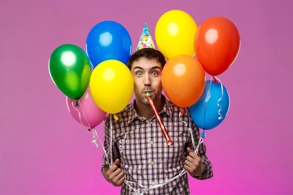 Homem engraçado segurando balões de aniversário e assoprando língua de sogra