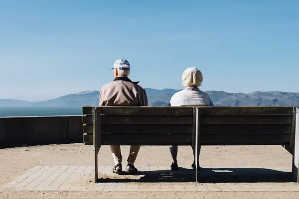 Casal de idosos sentados no banco observando uma paisagem de montanhas