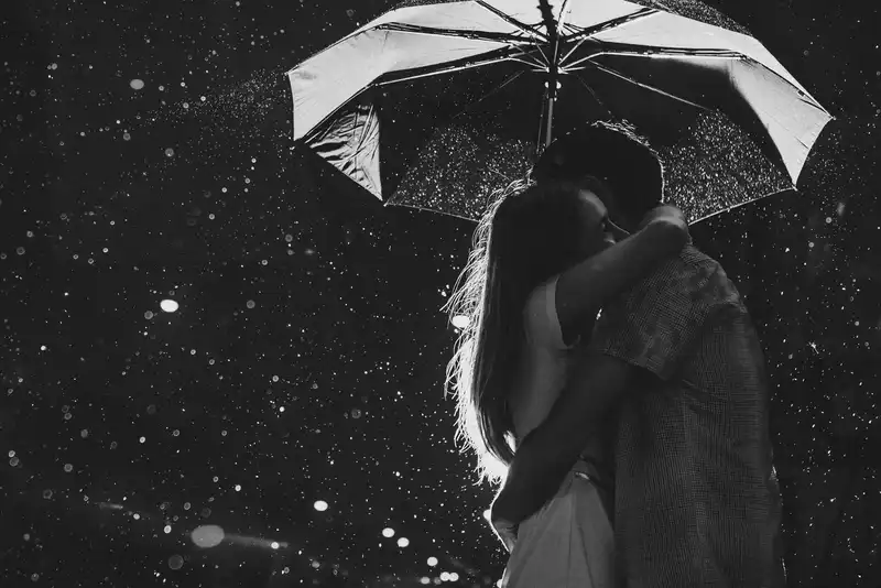 Foto em preto e branco de casal se abraçando debaixo de um guarda chuva