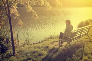 Mulher sozinha sentada no banco em frente a um lago
