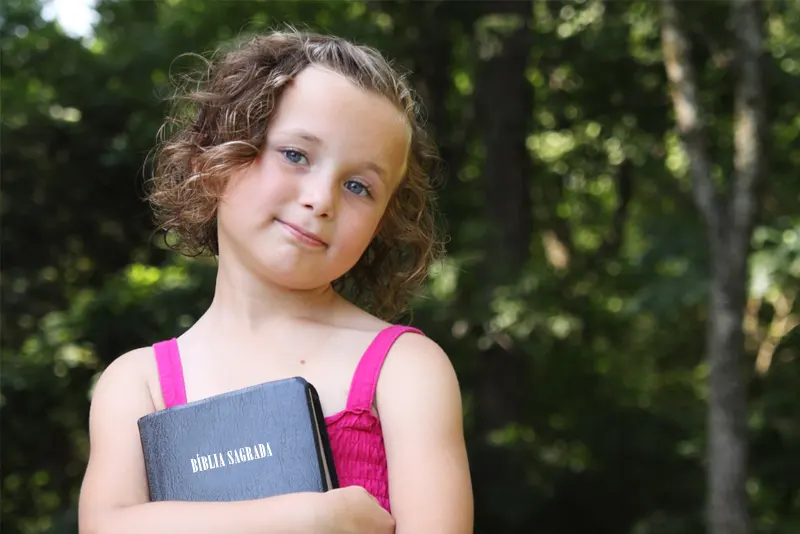 Menina de cabelo cacheado e vestido rosa segurando uma bíblia