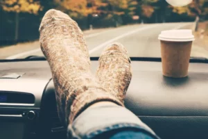 Pessoa com os pés no painel do carro e uma xícara de café