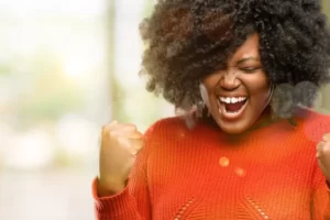 Mulher negra com blusa laranja comemorando vitória