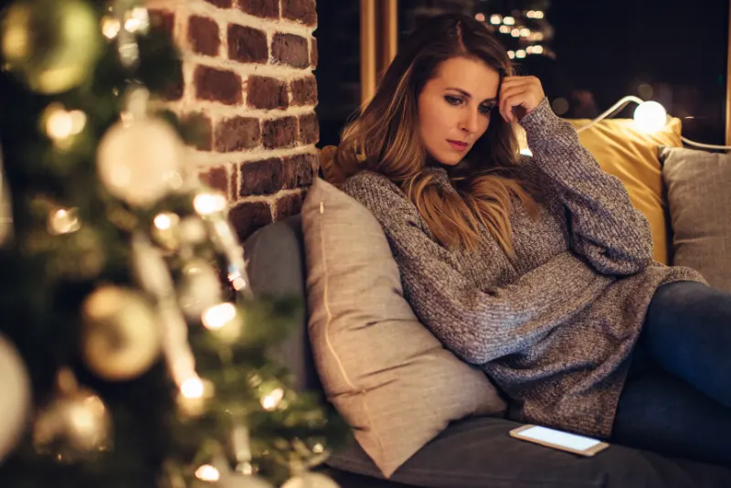 Mulher sentada sozinha no sofá triste durante o natal