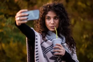 Mulher tirando selfie bebendo refrigerante de canudinho