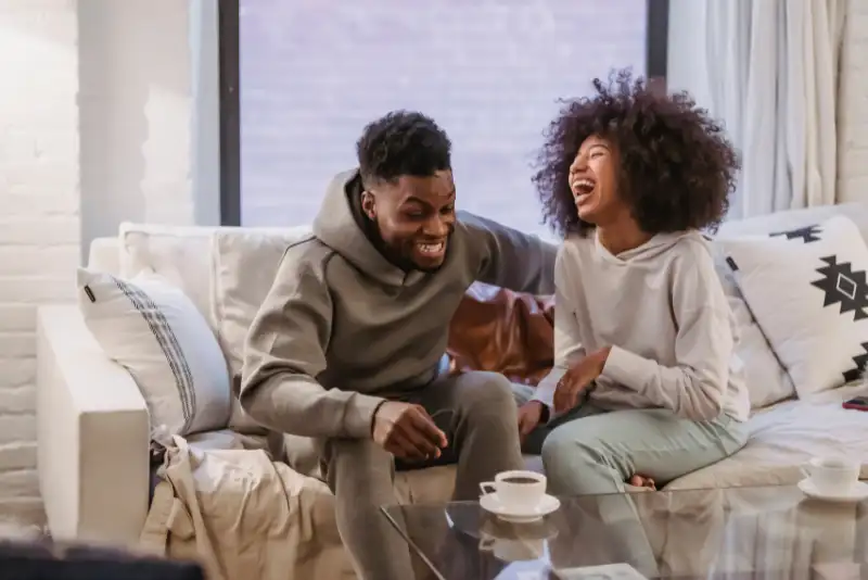 Casal afro se divertindo no sofá da sala - Ideias de atividades divertidas para casais