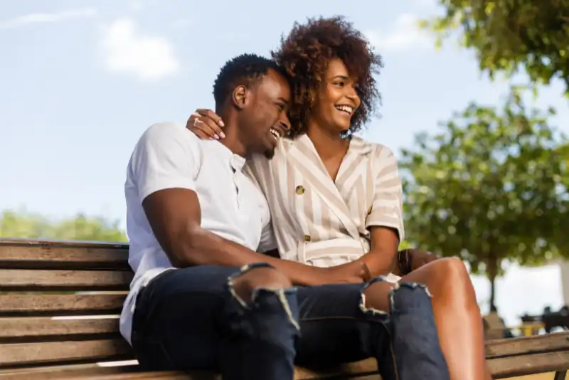 Casal negro sentado no banco ao ar livre e rindo