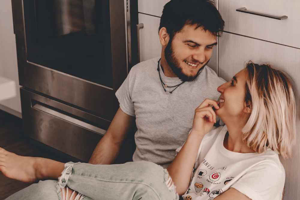Casal enconstado no balcão da cozinha, conversando e rindo - Encontrar Sua Alma Gêmea