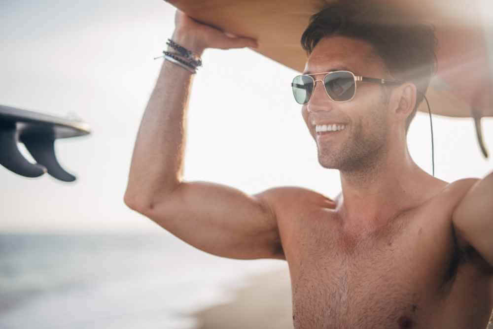 Homem sorrindo carregando uma prancha de surf