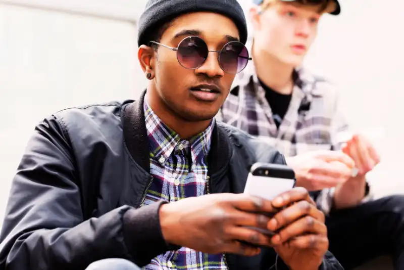 Menino de touca e jaqueta de couro mexendo no celular