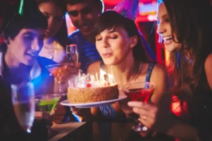 Mulher apagando as velinhas do bolo juntamente com seus amigos comemorando seu aniversário