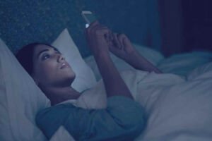 Mulher deitada na cama mexendo no celular