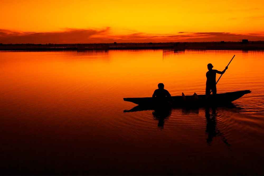 Silhueta de dois homens pescando em um barco ao por do sol