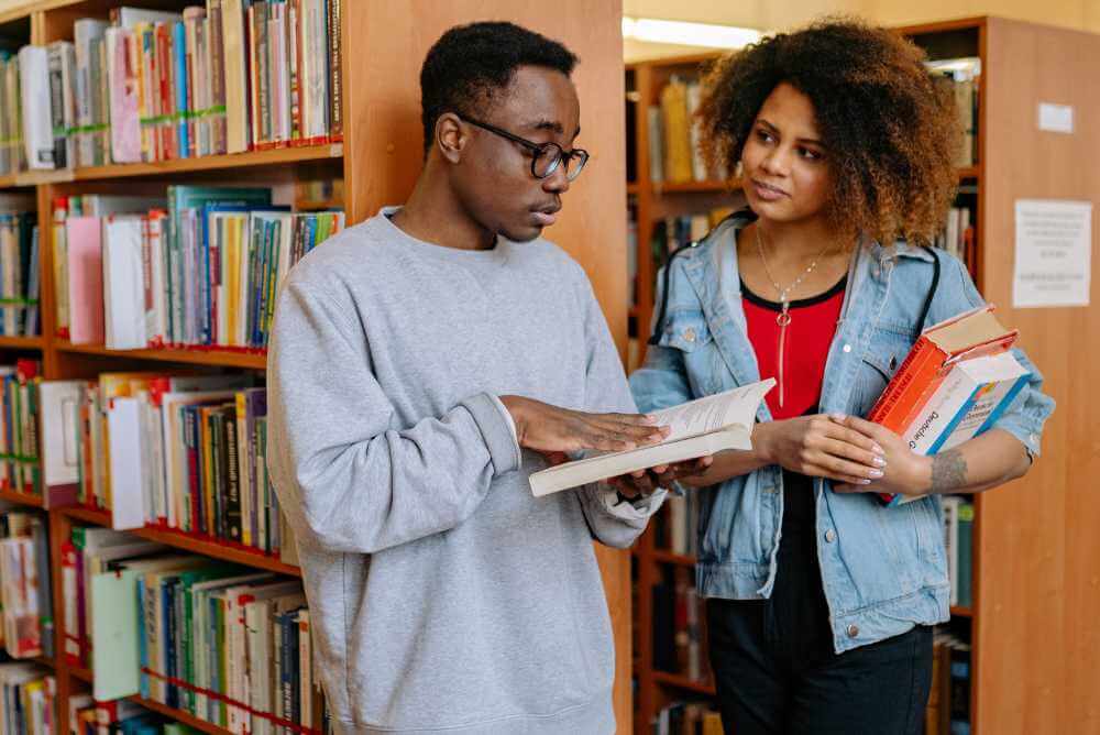 Dois jovens negros com livros em uma biblioteca