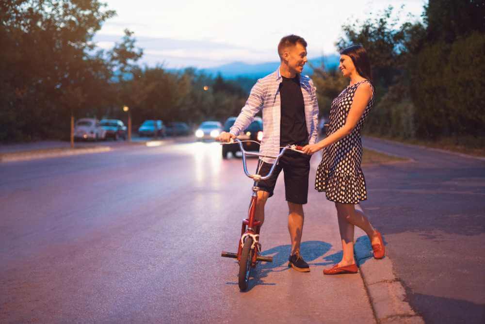Homem de bicicleta conversando com uma mulher de vestido de bolinha na rua - Flerte ou amizade