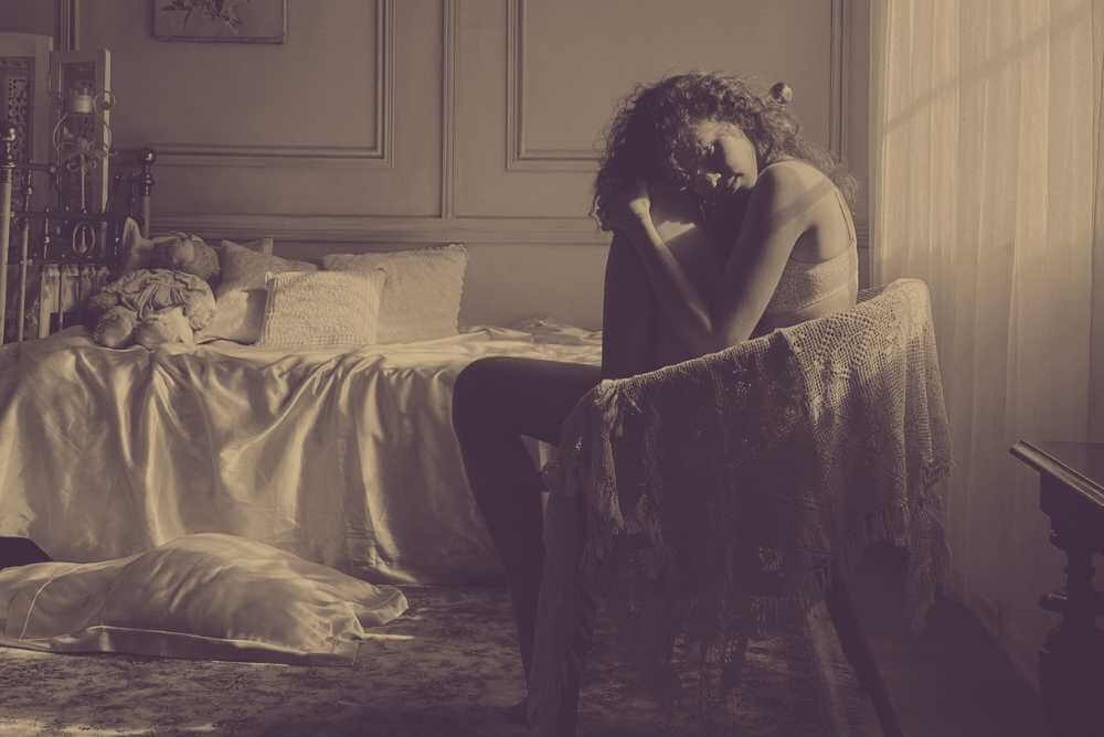 Mulher triste sentada numa cadeira em um quarto desarrumado