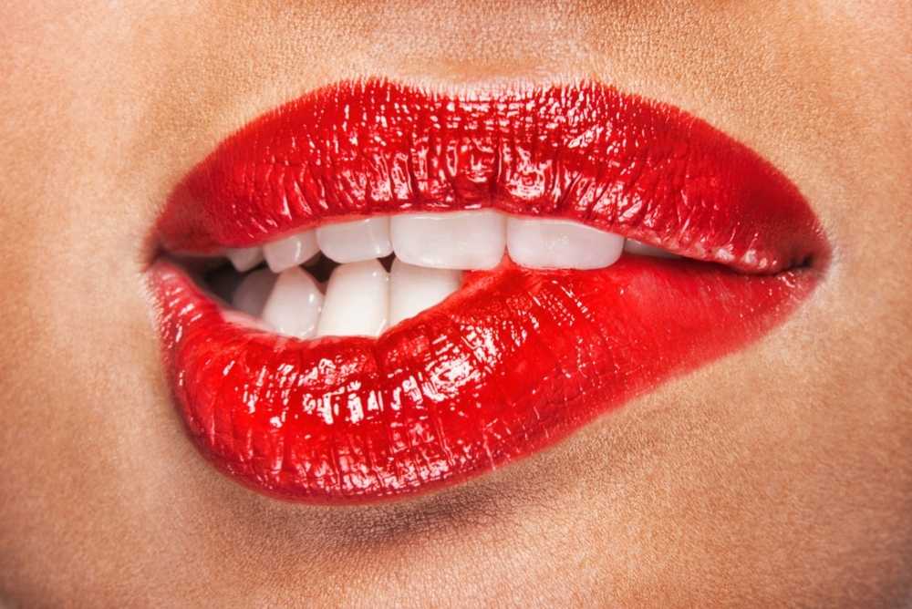 Mulher de batom vermelho mordendo o lábio expressando sensualidade feminina
