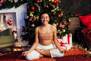 Mulher em posição de lótus em frente à uma árvore de natal meditando