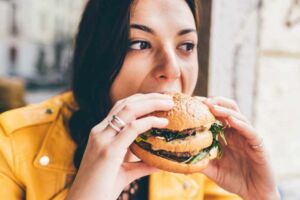 Mulher comendo um lanche e arregalando os olhos