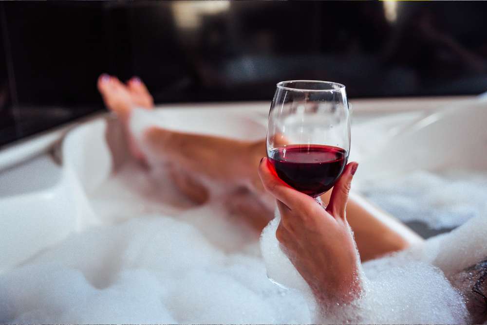 Mulher segurando uma taça de vinho dentro de uma banheira