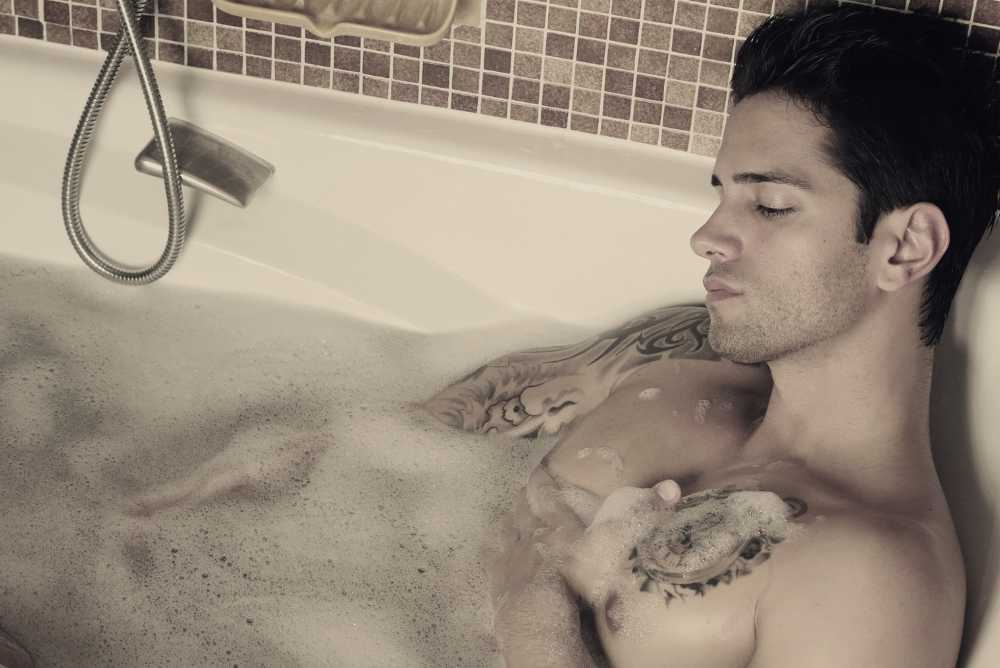 Homem sexy com tatuagens triste dentro de uma banheira