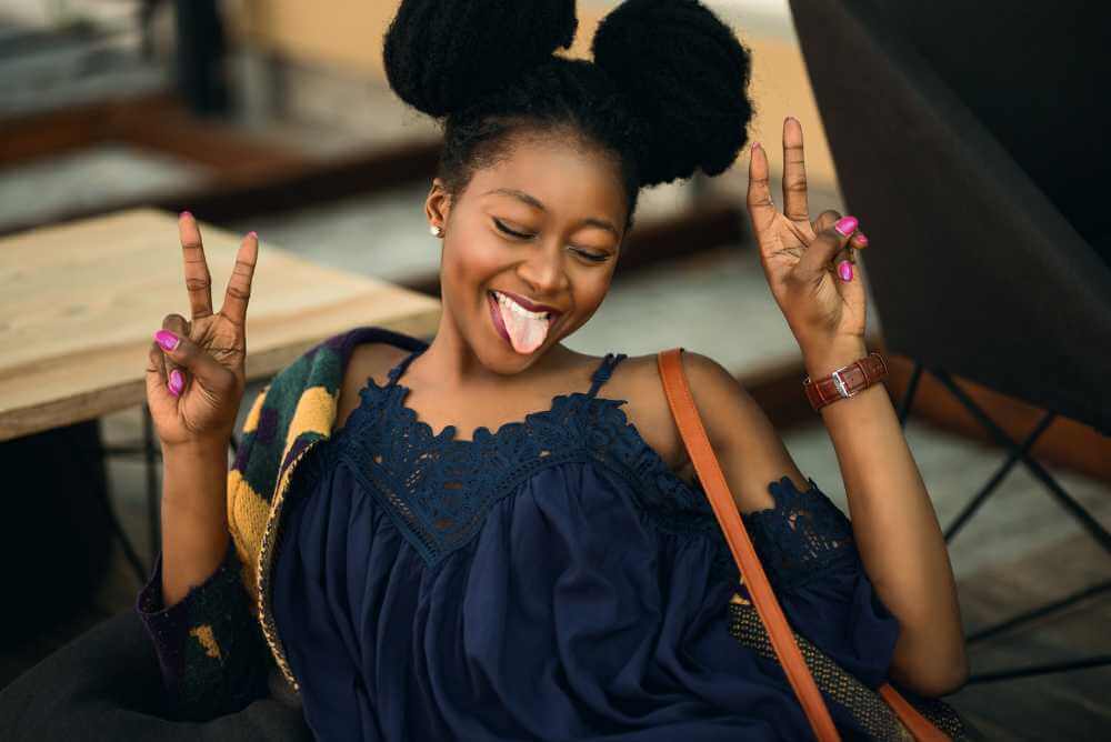 Mulher negra sorrindo e fazendo v de vitória com as mãos