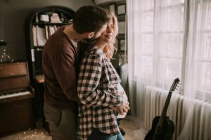 Homem abraçando sua esposa grávida na sala com violão encostado na parede